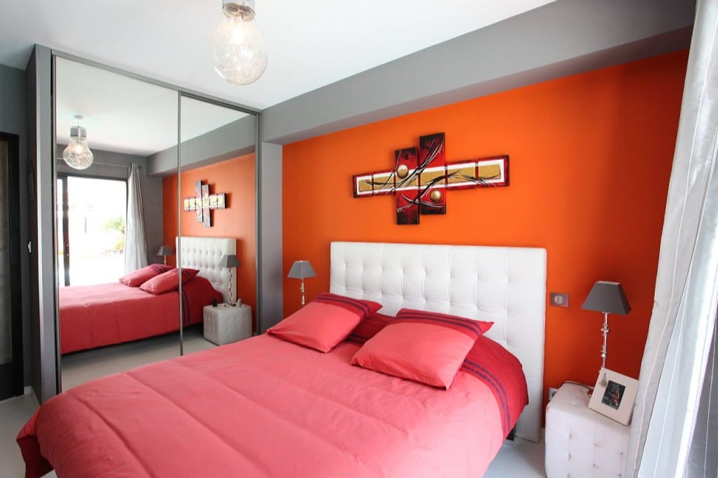 Chambre moderne colorée orange avec lit double et miroir mural